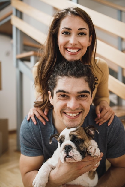 Ritratto di una giovane coppia sorridente con il loro cucciolo di bulldog inglese mentre si trasferisce nella loro nuova casa. Guardando la fotocamera.