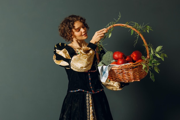 Ritratto di una giovane donna adulta vestita con un abito medievale che tiene in mano un cesto con verdure e frutta