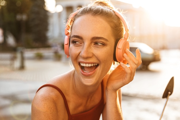 Ritratto di una giovane donna affascinante che ascolta musica con cuffie wireless mentre è seduta su uno scooter all'aperto sulla strada della città