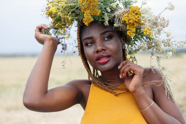 Ritratto di una giovane donna afroamericana, modella di moda, con grandi fiori tra i capelli. Ritratto di una ragazza in un piano storto in un campo con fiori. corona sulla sua testa on