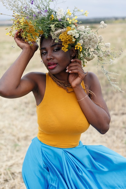 Ritratto di una giovane donna afroamericana, modella di moda, con grandi fiori tra i capelli. Ritratto di una ragazza in un piano storto in un campo con fiori. corona sulla sua testa on