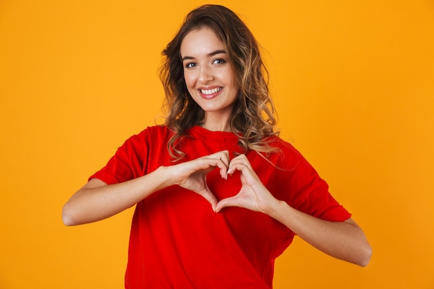 Ritratto di una giovane donna allegra adorabile in piedi isolata sul muro giallo, mostrando il gesto del cuore heart