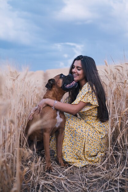 Ritratto di una giovane donna allegra che si diverte e si gode la natura con il suo cane in un campo di grano.