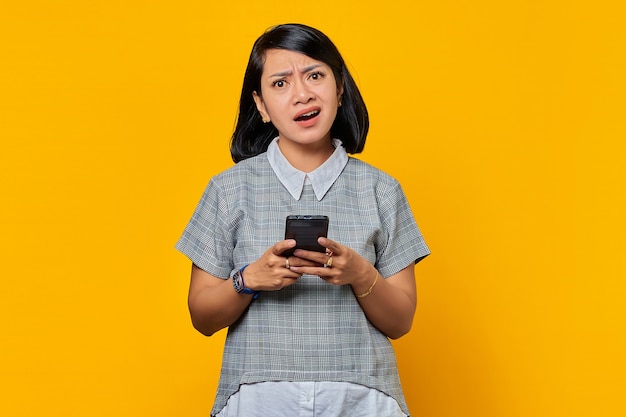 Ritratto di una giovane donna asiatica infelice che tiene il telefono cellulare e guarda la telecamera