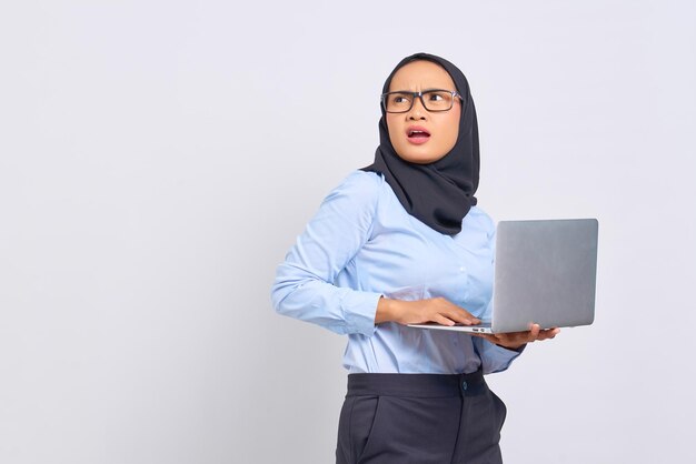 Ritratto di una giovane donna asiatica scioccata che tiene in mano un laptop e guarda lontano isolato su sfondo bianco