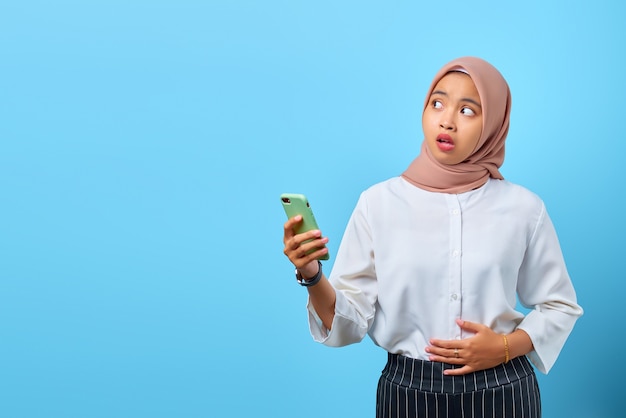Ritratto di una giovane donna asiatica scioccata con la bocca aperta che tiene il telefono cellulare mentre guarda di traverso