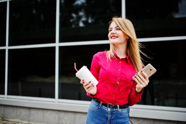 Ritratto di una giovane donna attraente che posa con il caffè e lo smartphone fuori del centro commerciale.