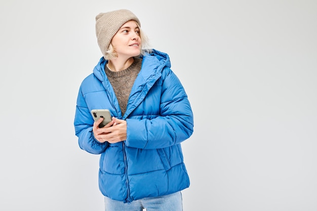 Ritratto di una giovane donna bionda con una giacca blu che tiene in mano un cellulare con una faccia sorridente felice Persona con uno smartphone isolato su uno sfondo bianco