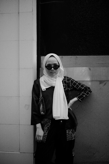 Ritratto di una giovane donna che indossa occhiali da sole in piedi contro il muro