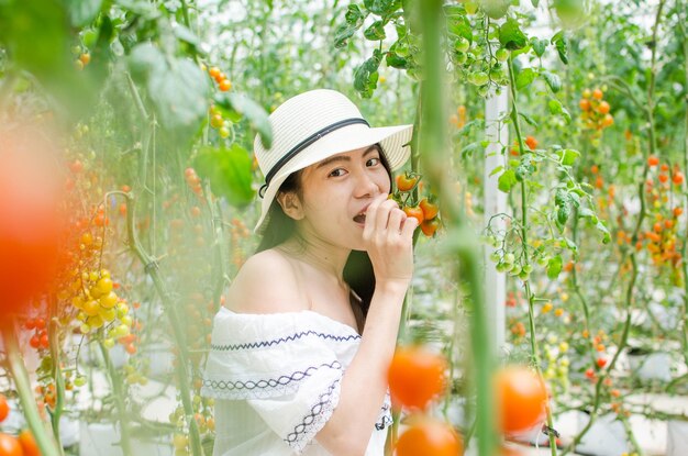 Ritratto di una giovane donna che indossa un cappello e mangia un pomodoro di ciliegio