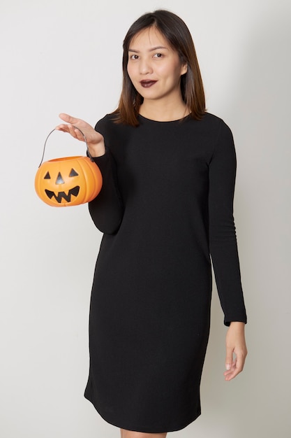 Ritratto di una giovane donna che indossa un costume da strega nera tiene una zucca per una festa di Halloween felice.