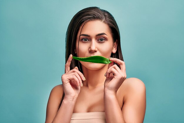 Ritratto di una giovane donna che tiene una foglia di aloe vera e nasconde un sorriso Il concetto di cosmetici