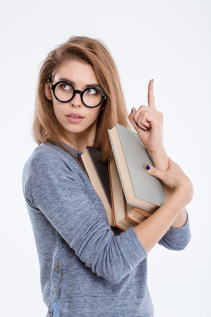 Ritratto di una giovane donna con gli occhiali che tiene libri e punta il dito verso l'alto isolato su uno sfondo bianco