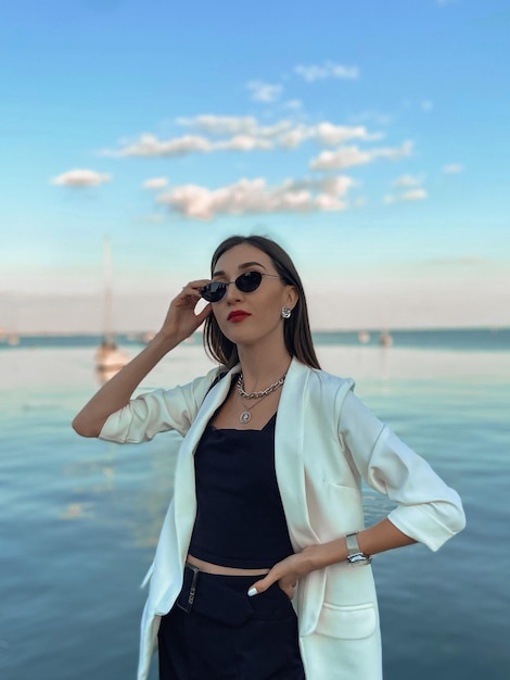 Ritratto di una giovane donna con gli occhiali da sole in piedi contro il mare