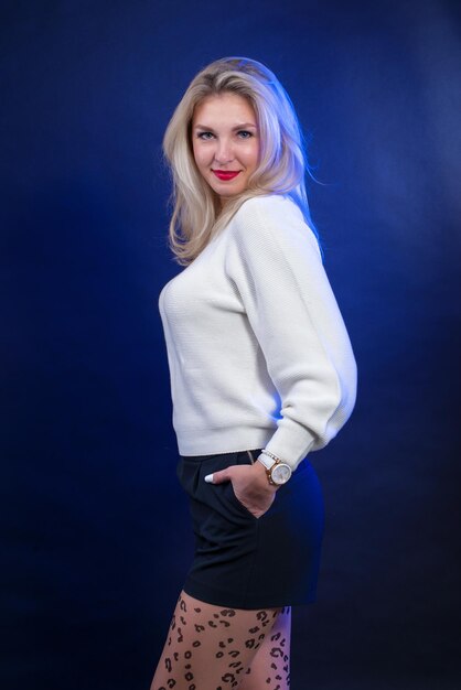 Ritratto di una giovane donna con i capelli biondi in un maglione bianco su sfondo blu in studio