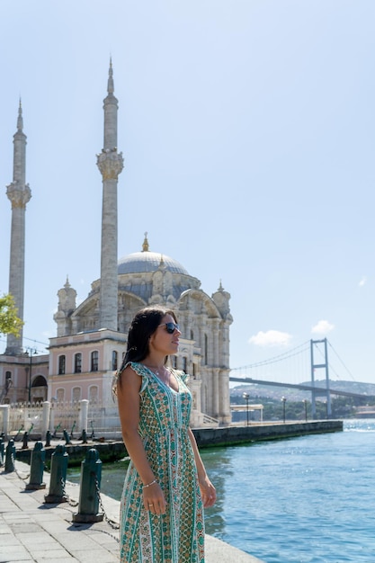Ritratto di una giovane donna con occhiali da sole in posa davanti alla moschea di Ortakoy e al famoso ponte di Istanbul