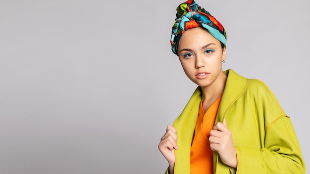 Ritratto di una giovane donna con trucco luminoso e un foulard alla moda. Sfondo chiaro. Bellezza, moda, concetto di trucco. ragazza in un cappotto verde brillante, vestito arancione brillante. Formato panoramico 16:9.