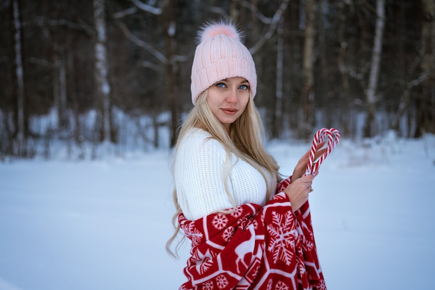 Ritratto di una giovane donna con un cappello rosa avvolto in un plaid rosso all'aperto in inverno con lecca-lecca