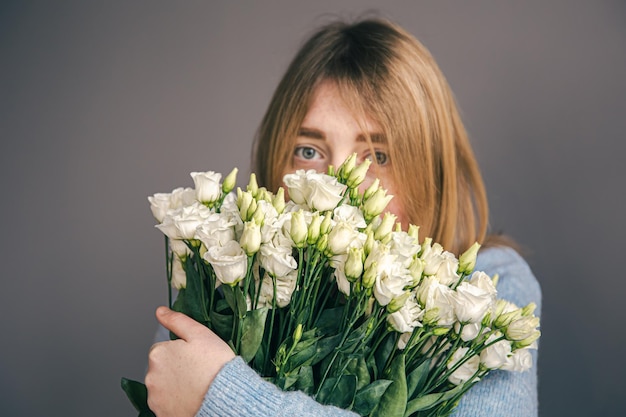 Ritratto di una giovane donna con un mazzo di rose su sfondo grigio