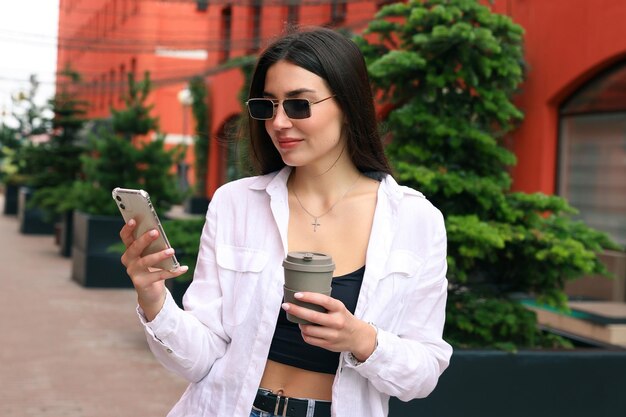 Ritratto di una giovane donna con un telefono e una tazza di caffè nel cortile dell'ufficio