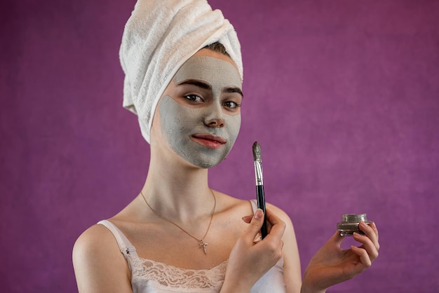 Ritratto di una giovane donna con una maschera di argilla verde sul viso isolata su viola