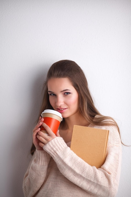 Ritratto di una giovane donna con una tazza di tè o caffè tenendo il libro