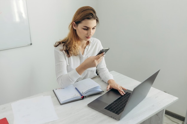 Ritratto di una giovane donna d'affari guardando il telefono Lavora a un computer nel suo ufficio a casa