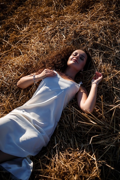 Ritratto di una giovane donna dai capelli ricci in un campo di grano, dove il grano viene falciato mentre si gode la natura. Natura. I raggi del sole. Agricoltura. Messa a fuoco selettiva