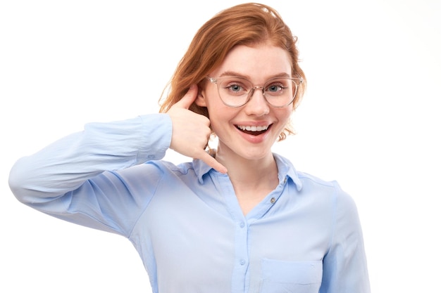 Ritratto di una giovane donna dai capelli rossi che finge di chiamare qualcuno fa il segno del gesto di chiamarmi con le dita isolate su uno sfondo bianco dello studio Dammi una chiamata mano a forma di telefono