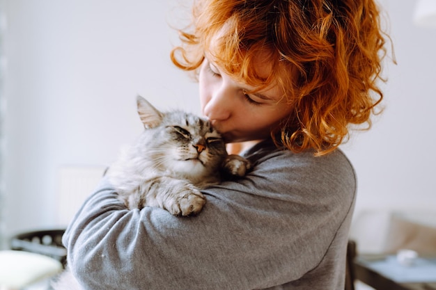Ritratto di una giovane donna dai capelli rossi e ricci con un amato gatto domestico peloso