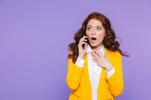 Ritratto di una giovane donna dai capelli rossi piuttosto confusa in piedi su viola, utilizzando il telefono cellulare