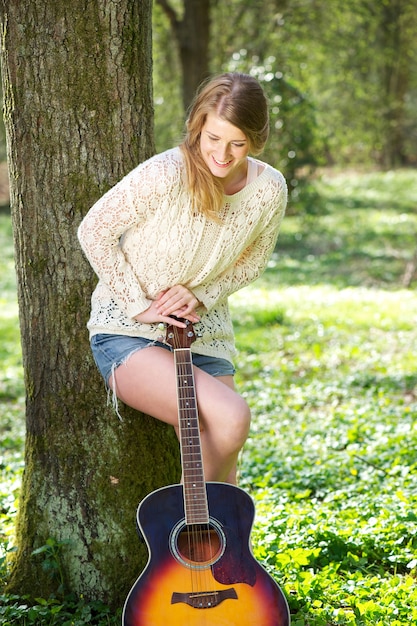 Ritratto di una giovane donna di relax con la chitarra sotto un albero