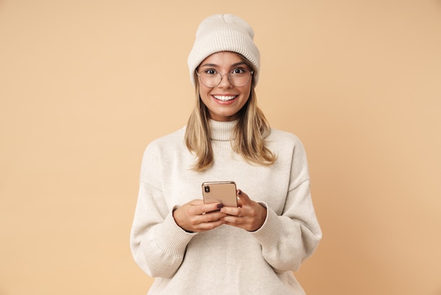 Ritratto di una giovane donna felice con gli occhiali che sorride e scrive sullo smartphone