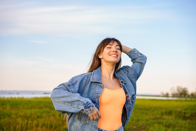 Ritratto di una giovane donna felice con i capelli lunghi, in jeans su uno sfondo di cielo ballando