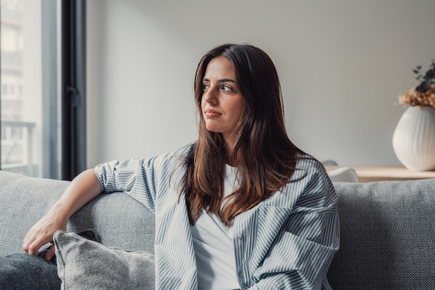 Ritratto di una giovane donna felice e sognante che guarda lontano, in piedi con le braccia piegate in un salotto moderno, visualizzando il futuro, ricordando buoni ricordi, pianificando il fine settimana o pensando a soluzioni ai problemi.