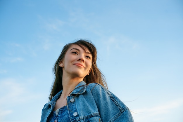 Ritratto di una giovane donna felice in giacca di jeans sullo sfondo del cielo