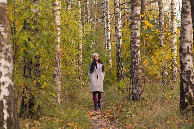 Ritratto di una giovane donna gioiosa che gode nel parco autunnale. Bella ragazza castana in cappotto grigio di autunno e cappello lavorato a maglia. Rilassati nella natura.