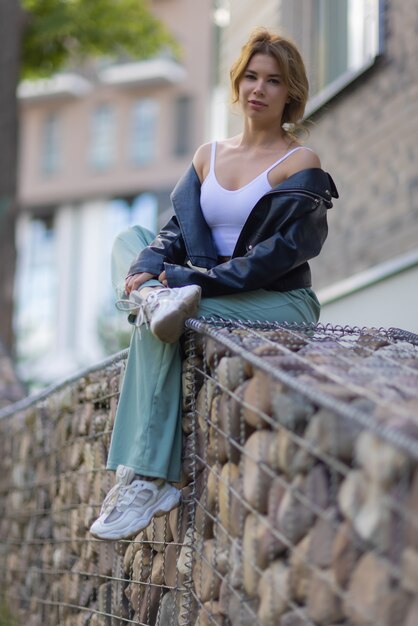 Ritratto di una giovane donna graziosa in pantaloncini blu seduta su una panchina nel cortile di un complesso residenziale.