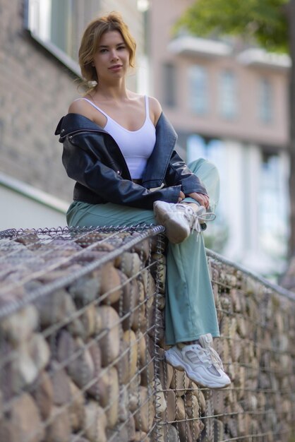 Ritratto di una giovane donna graziosa in pantaloncini blu seduto su una panchina nel cortile di un com residenziale