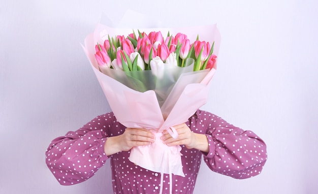 Ritratto di una giovane donna in abito viola azienda bouquet di tulipani rosa e bianchi su grigio. Cartolina d'auguri di primavera. Pasqua, concetto di fiore di primavera. Festa della mamma o della donna.