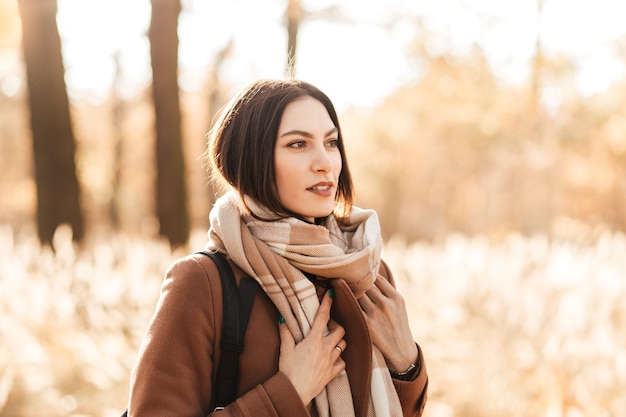 Ritratto di una giovane donna in cappotto e sciarpa in autunno nel parco