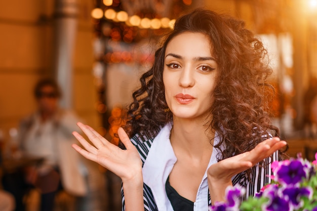 Ritratto di una giovane donna in un caffè per strada seduto a un tavolo allargando le mani a lato