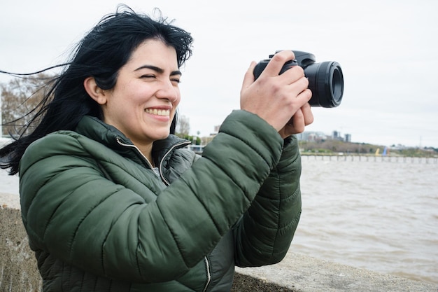 ritratto di una giovane donna latina che sorride prendendo una foto con la sua fotocamera digitale DSLR