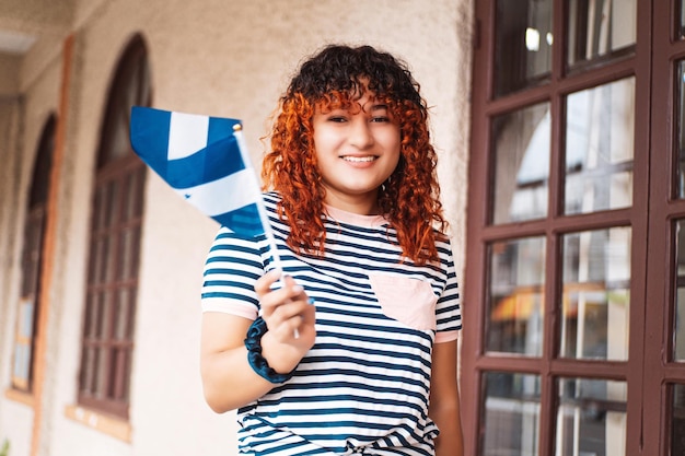 Ritratto di una giovane donna latinoamericana con capelli colorati che guarda l'obbiettivo e tiene e sventola una piccola bandiera dell'honduras