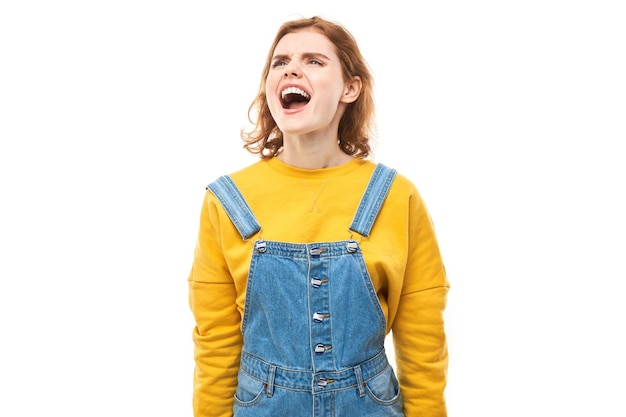 Ritratto di una giovane donna rossa arrabbiata che urla isolata sullo sfondo bianco dello studio che mostra emozioni negative.
