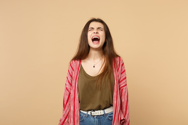 Ritratto di una giovane donna selvaggia pazza in abiti casual che tiene gli occhi chiusi, urlando isolato su sfondo beige pastello in studio. Persone sincere emozioni, concetto di stile di vita. Mock up copia spazio.