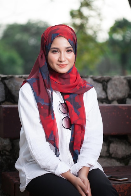 Ritratto di una giovane donna sorridente che indossa l'hijab mentre è seduta su una panchina