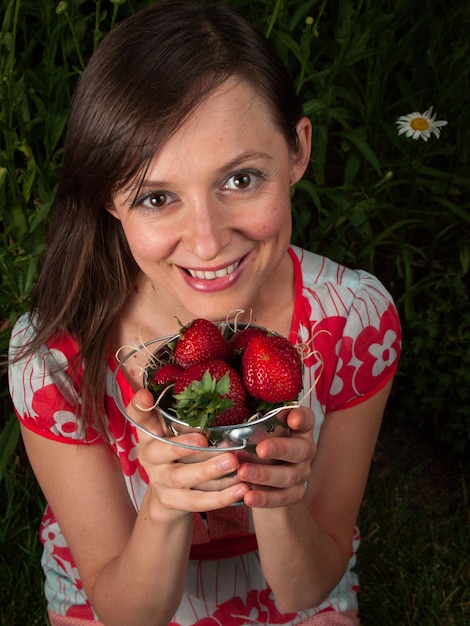 Ritratto di una giovane donna sorridente che tiene le fragole.