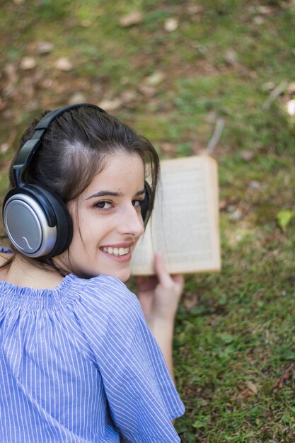 Ritratto di una giovane donna sorridente che tiene un libro sdraiato sull'erba