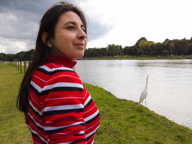 Ritratto di una giovane donna sorridente in piedi vicino al lago contro il cielo